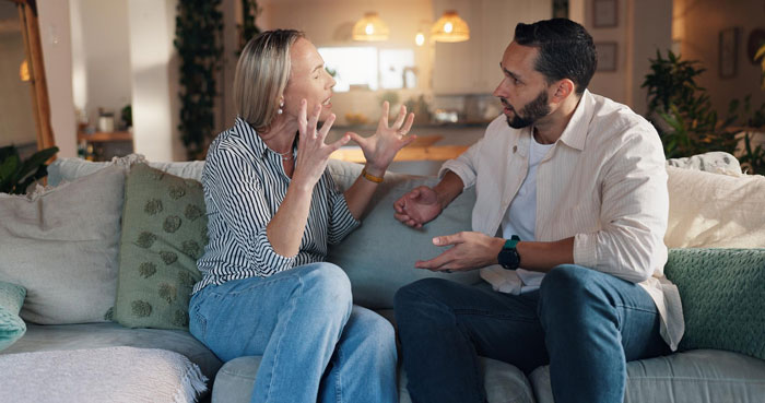 Couple having a heated discussion on couch, highlighting sister relationship cheater tension in a home setting.
