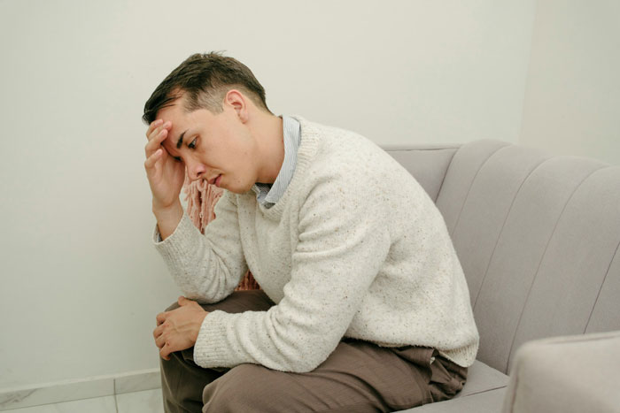 Widowed dad sitting on couch looking stressed, reflecting on teen daughter&rsquo;s jealousy affecting his new love life.