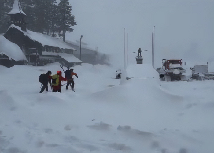 Six mothers in winter clothing walking through deep snow near a snowy village scene after enjoying time off together.