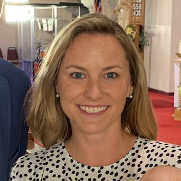 Smiling mother with blonde hair, wearing a white and black polka dot shirt, captured indoors during a gathering.