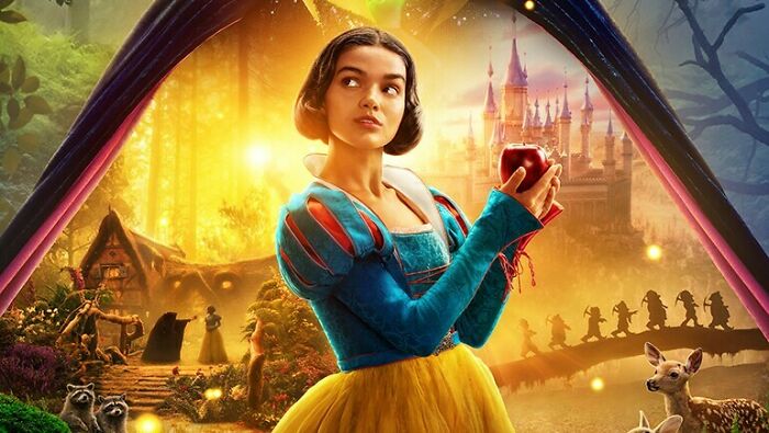 Live-action Snow White holding an apple in a colorful forest scene with animals and a castle in the background.