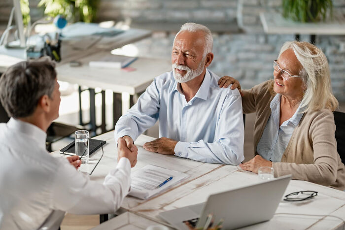 Senior couple shaking hands with a lawyer in an office, discussing legal information that surprised them during consultation.
