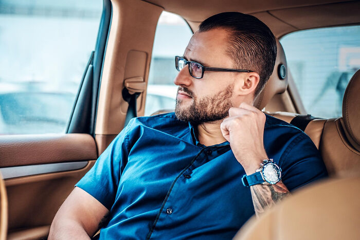 Man with glasses in a blue shirt sitting in a car, reflecting thoughtfully on surprising lawyer information.