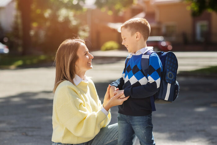 Woman kneeling and talking to a young boy with a backpack outside, illustrating lawyers confessing surprising information.