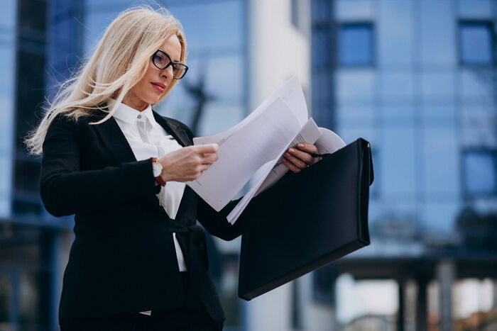 Professional lawyer with glasses reviewing legal documents outdoors near office building, focused on important case information.