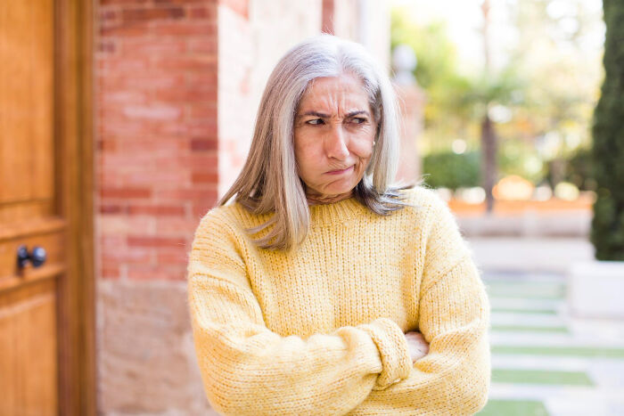 Older woman in yellow sweater with arms crossed and doubtful expression, reflecting lawyers reacting to surprising information.