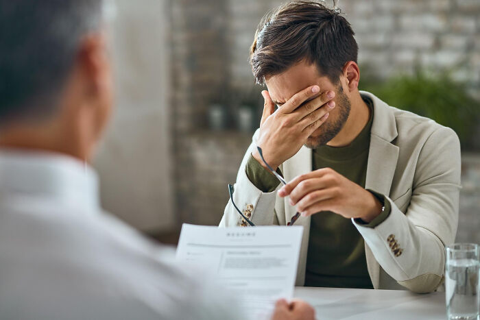Stressed man in business attire holding glasses while reacting to surprising legal information during a consultation session.