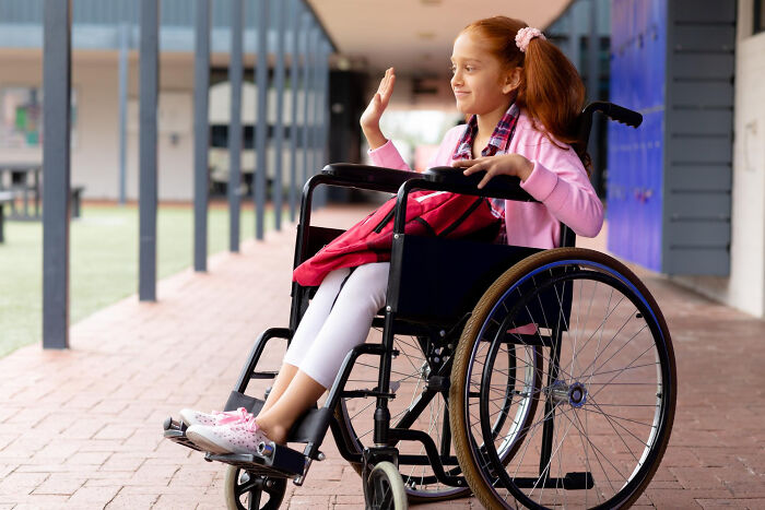 Young girl in a wheelchair smiling and waving in a school hallway, illustrating a story about lawyers' surprising information.