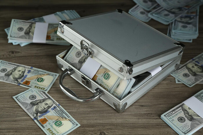 Silver briefcase filled with stacks of US hundred-dollar bills on a wooden surface related to lawyers’ shocking information.