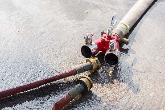 Fire hoses connected to a red valve lying on wet ground, illustrating emergency equipment and legal safety regulations.