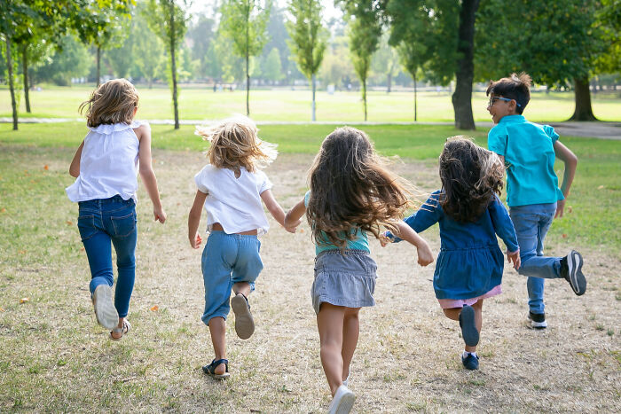 Five children running in a park on a sunny day, capturing a joyful moment of play and movement outdoors.