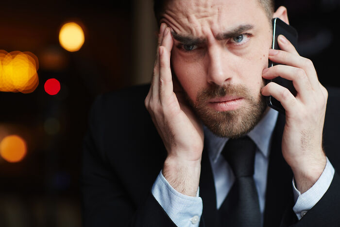 Stressed lawyer in suit holding phone to ear with worried expression during a tense conversation in dim light.