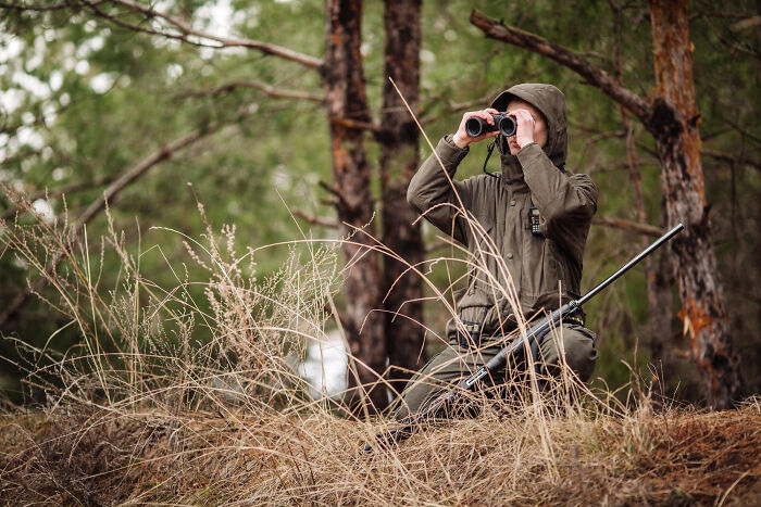 Lawyer in outdoor gear using binoculars in a forest setting, symbolizing lawyers confessing surprising information.