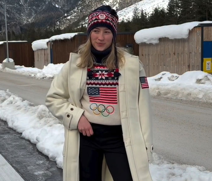 Female athlete wearing USA Winter Olympics sweater and hat, standing in snowy outdoor setting during 2026 Winter Olympics.
