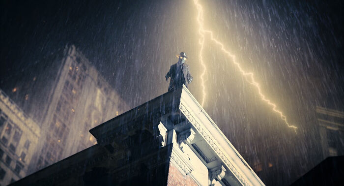 Spider-Noir standing on a rooftop in rain with lightning striking in the dark city, showcasing his mysterious powers.