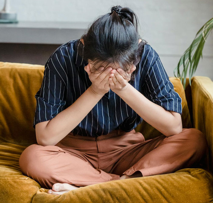 Woman sitting on couch with face in hands looking stressed, related to couple suspecting step-mom food theft incident.