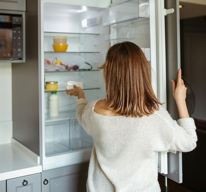 Woman checking mostly empty fridge shelves, illustrating food theft by step-mom suspected in couple's dispute.