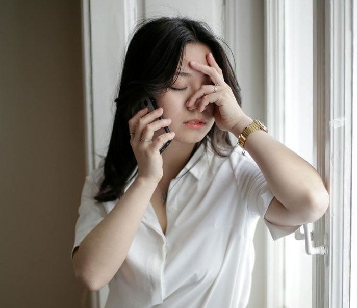 Stressed woman on phone near window, reacting to food theft by wife's step-mom causing couple's CPS visit concerns.