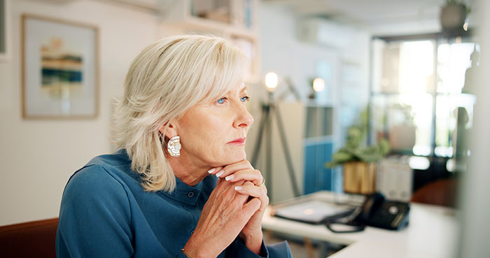 Pensive mature woman sitting indoors, reflecting on stepdaughters cheating, lies, and a broken relationship.