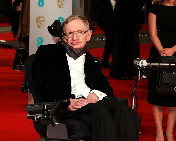 Stephen Hawking em um evento no tapete vermelho, vestido formalmente, enquanto a família se dirige a Epstein registrando reações fotográficas. Stephen Hawking em um evento no tapete vermelho, vestido formalmente, enquanto a família se dirige a Epstein registrando reações fotográficas.