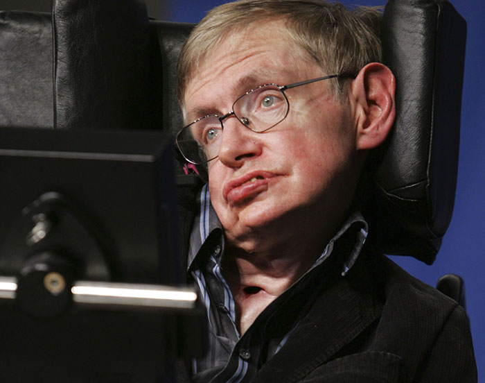 Stephen Hawking sentado em uma cadeira motorizada usando óculos e jaqueta escura durante uma aparição pública. Stephen Hawking sentado em uma cadeira motorizada usando óculos e jaqueta escura durante uma aparição pública.