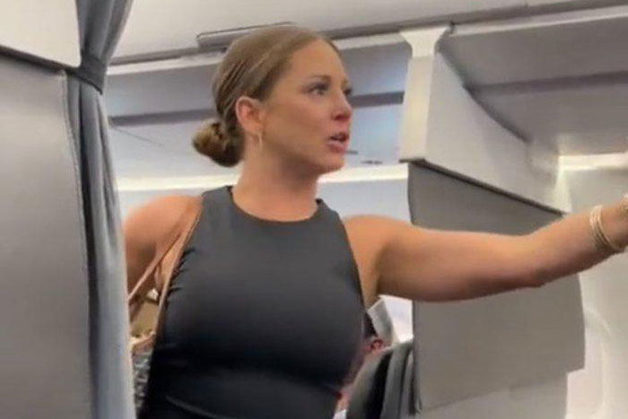 Woman in a black sleeveless top gesturing inside an airplane cabin, related to conspiracy theories discussion.