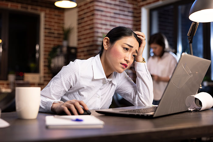 Woman looking frustrated while working on a laptop late at night, relating to conspiracy theories and alternative ideas.