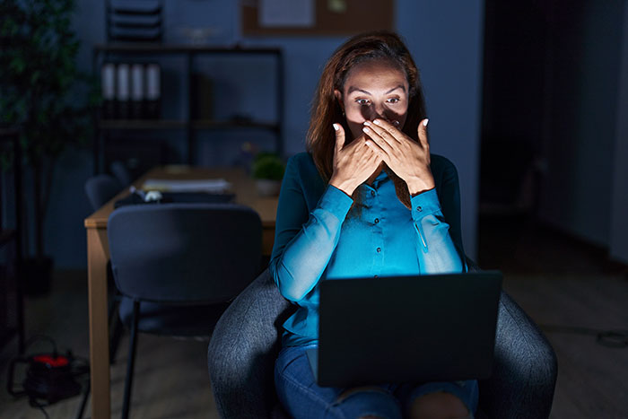 Woman in a dark room covering her mouth in shock while looking at a laptop screen researching conspiracy theories.