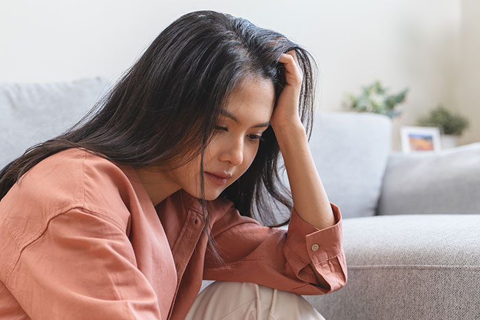 Young woman sitting on the floor in a living room looking worried, relating to younger sister trouble confession.