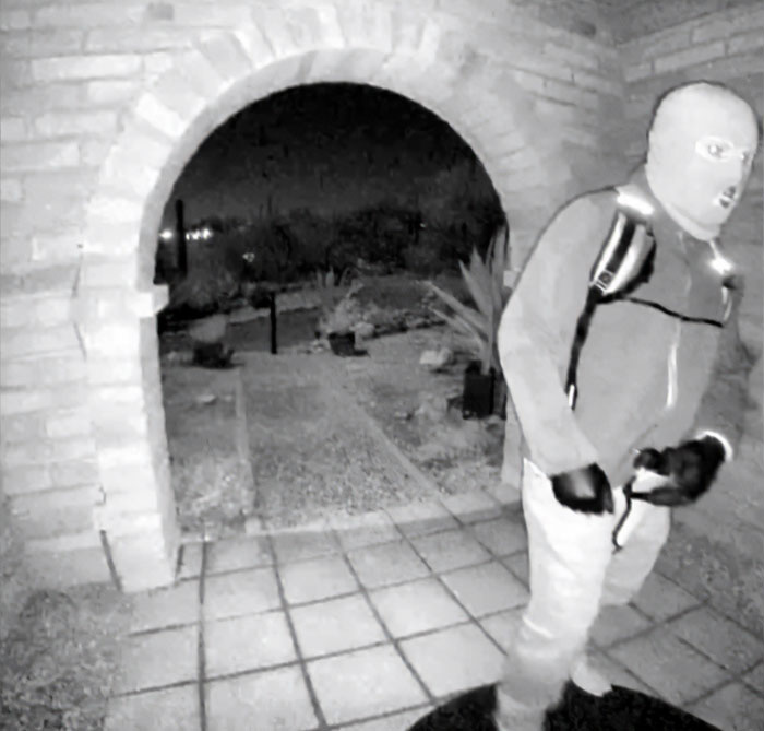 Man detained in connection with Nancy Guthrie kidnapping wearing mask and gloves near a brick archway at night.