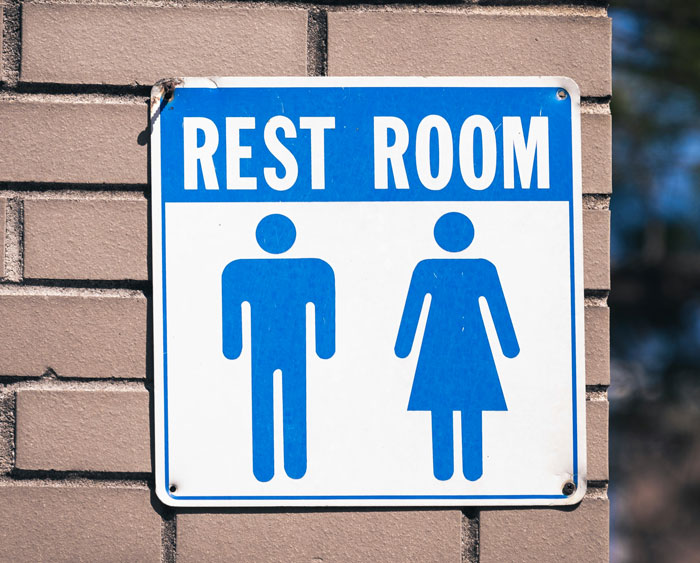 Restroom sign showing male and female symbols on a brick wall, related to dad bringing 3YO daughter inside men's toilet.
