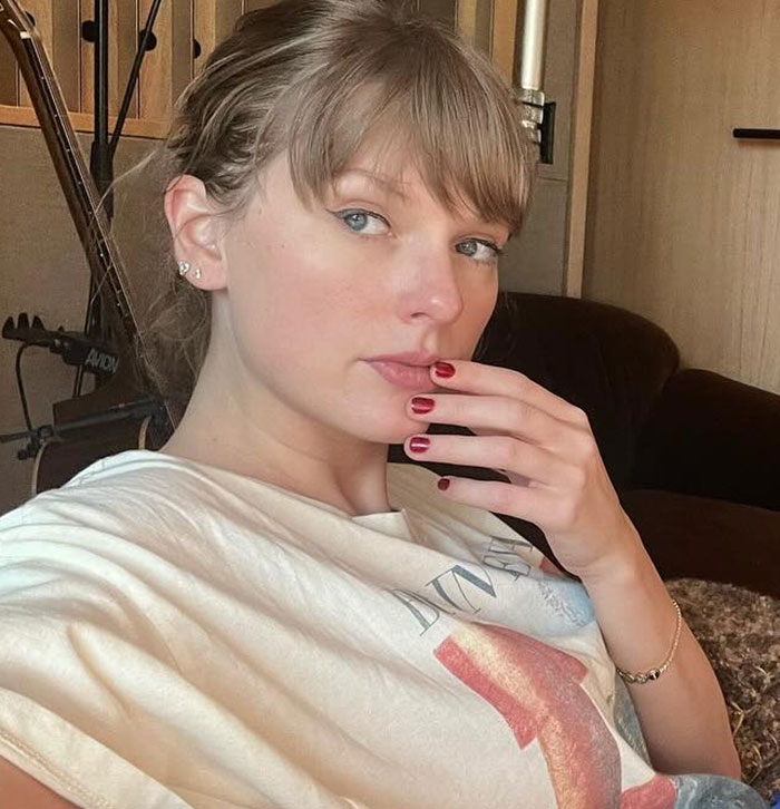 Taylor Swift posing indoors with hand near face, casual outfit, natural makeup sparking backlash over gift to Selena Gomez.