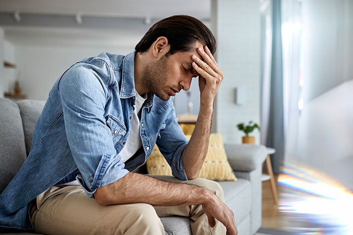 Man sitting on a couch holding his head in distress, reflecting on a teacher's malicious threats causing serious consequences.