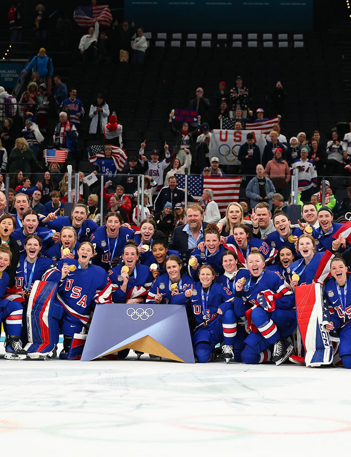 US Olympics women's hockey team celebrating victory on ice with gold medals and fans in the background. US Olympics women's hockey team celebrating victory on ice with gold medals and fans in the background.