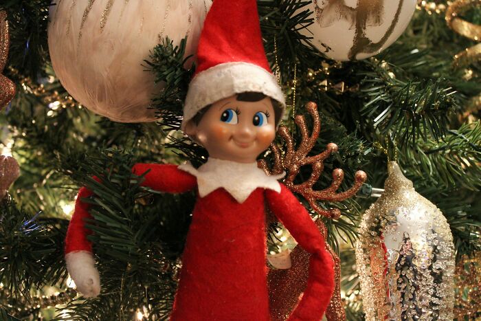 Elf doll in a red suit on a decorated Christmas tree, sparking funny and harmless conspiracy theories humor.