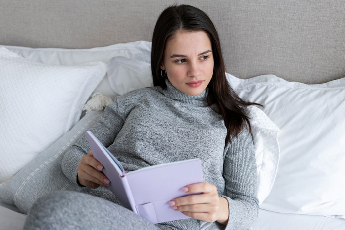 Woman in gray sweater reading a book on bed, reflecting on therapy funding and its impact on her marriage.