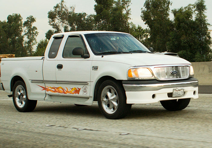 White Ford pickup truck with flame decals driving on a highway, representing behaviors linked to a man-child.