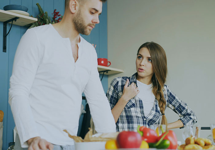 Young woman confronting man-child behavior in a kitchen, showing signs of frustration during a serious conversation.