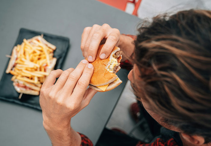 Man-child behavior shown by a guy eating a burger and fries in a casual setting, illustrating immature habits.
