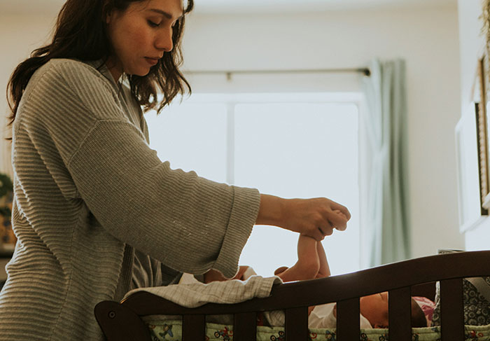 Woman gently holding baby's foot in a nursery, illustrating behaviors related to dealing with a man-child.