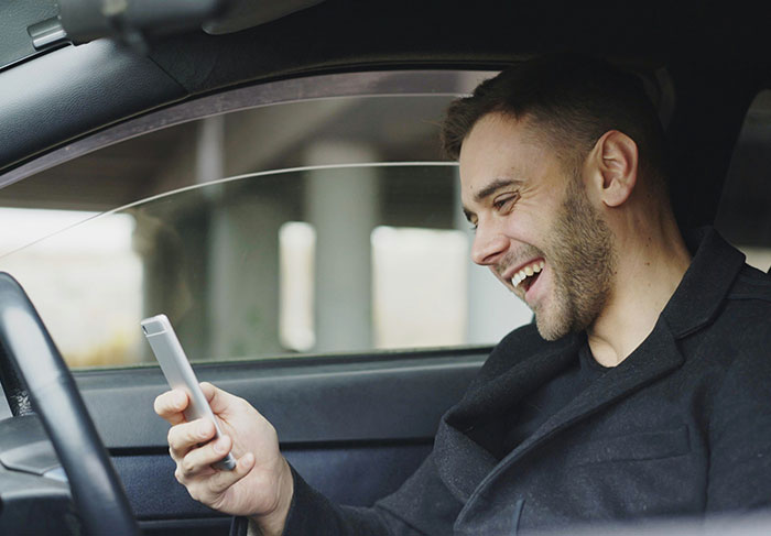 Man in car laughing at phone, illustrating common behaviors of a man-child in modern relationships.