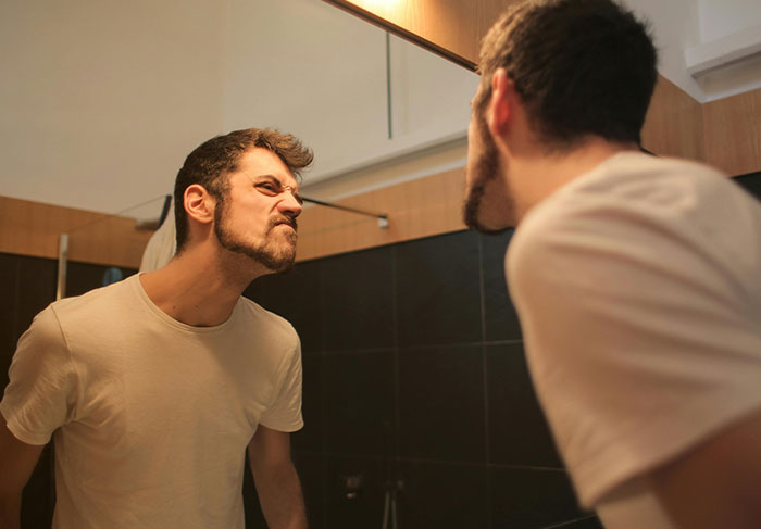 Man displaying immature behavior, making a frustrated face in the mirror, illustrating common signs of a man-child.