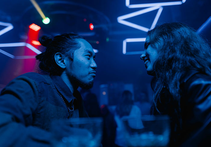 A man and woman talking closely in a dimly lit club, illustrating behaviors of a man-child in social settings.
