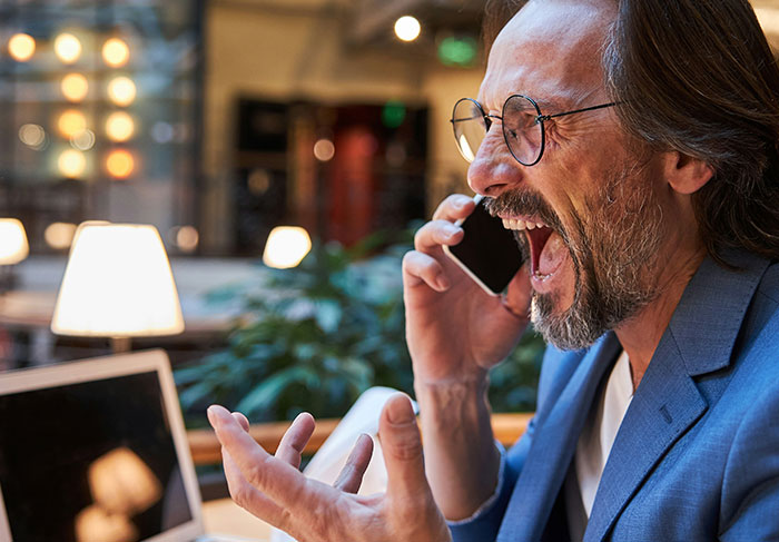 Man in glasses showing frustration on phone call in modern workspace, illustrating behaviors of a man-child.