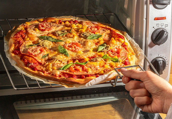 Hand taking a freshly baked pizza out of an oven, illustrating a cozy home moment related to man-child behaviors.