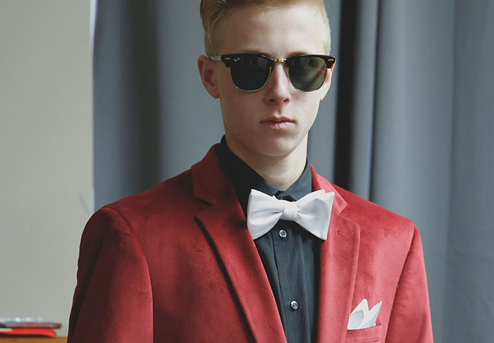 Young man in sunglasses and red blazer with white bow tie, representing behaviors of a man-child concept.