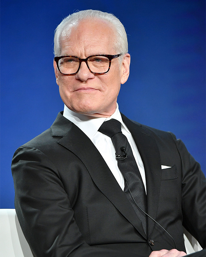 Tim Gunn wearing a black suit and glasses, speaking about the heartbreaking reason behind celibacy.
