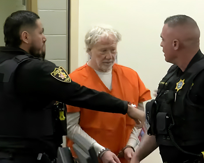 Timothy Busfield in orange prison uniform, handcuffed and escorted by officers in a serious child case situation.