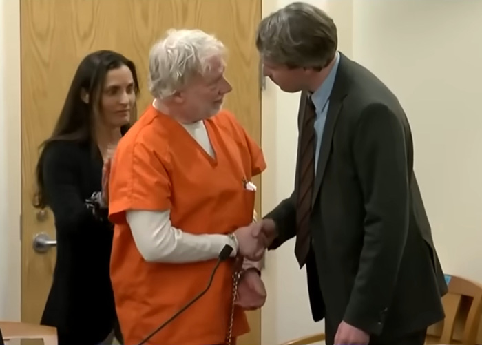 Timothy Busfield in orange prison jumpsuit shaking hands with lawyer amid serious charges in child case courtroom setting