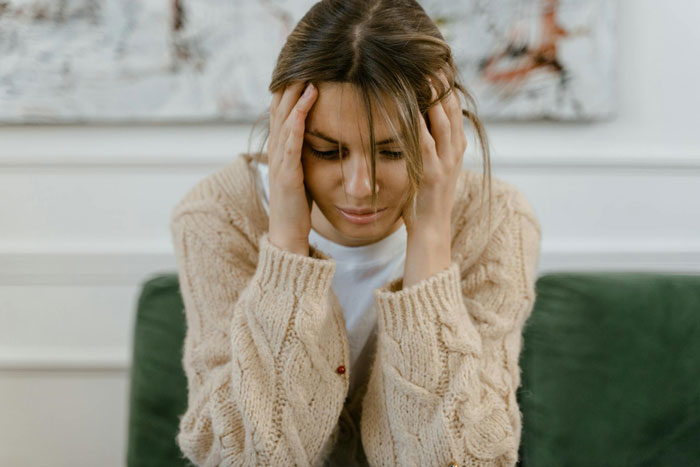 Tired woman in beige sweater sitting quietly with hands on her head, reflecting on marriage and quiet quit feelings.